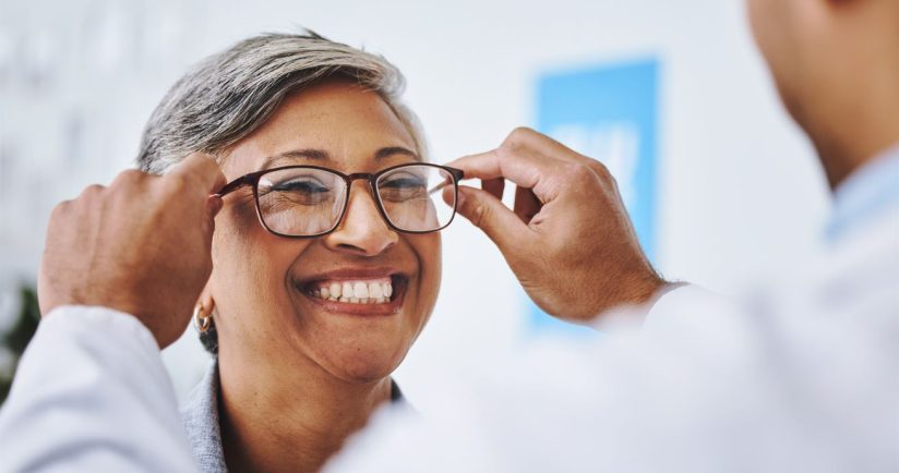 Eine lächelnde Person bekommt von einem Optiker eine Brille angepasst.